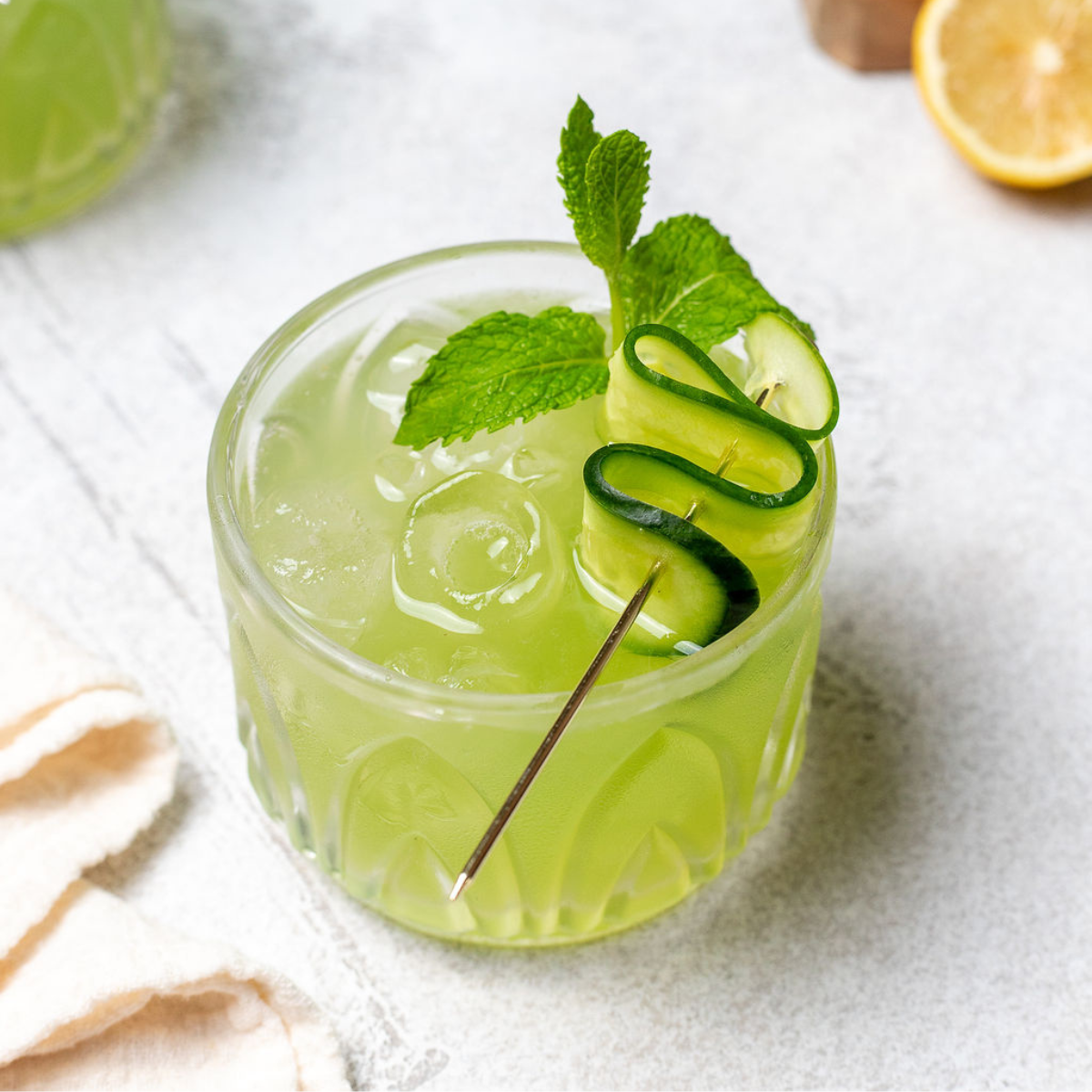 Cucumber cooler in a glass garnished with a cucumber ribbon and a sprig of mint.