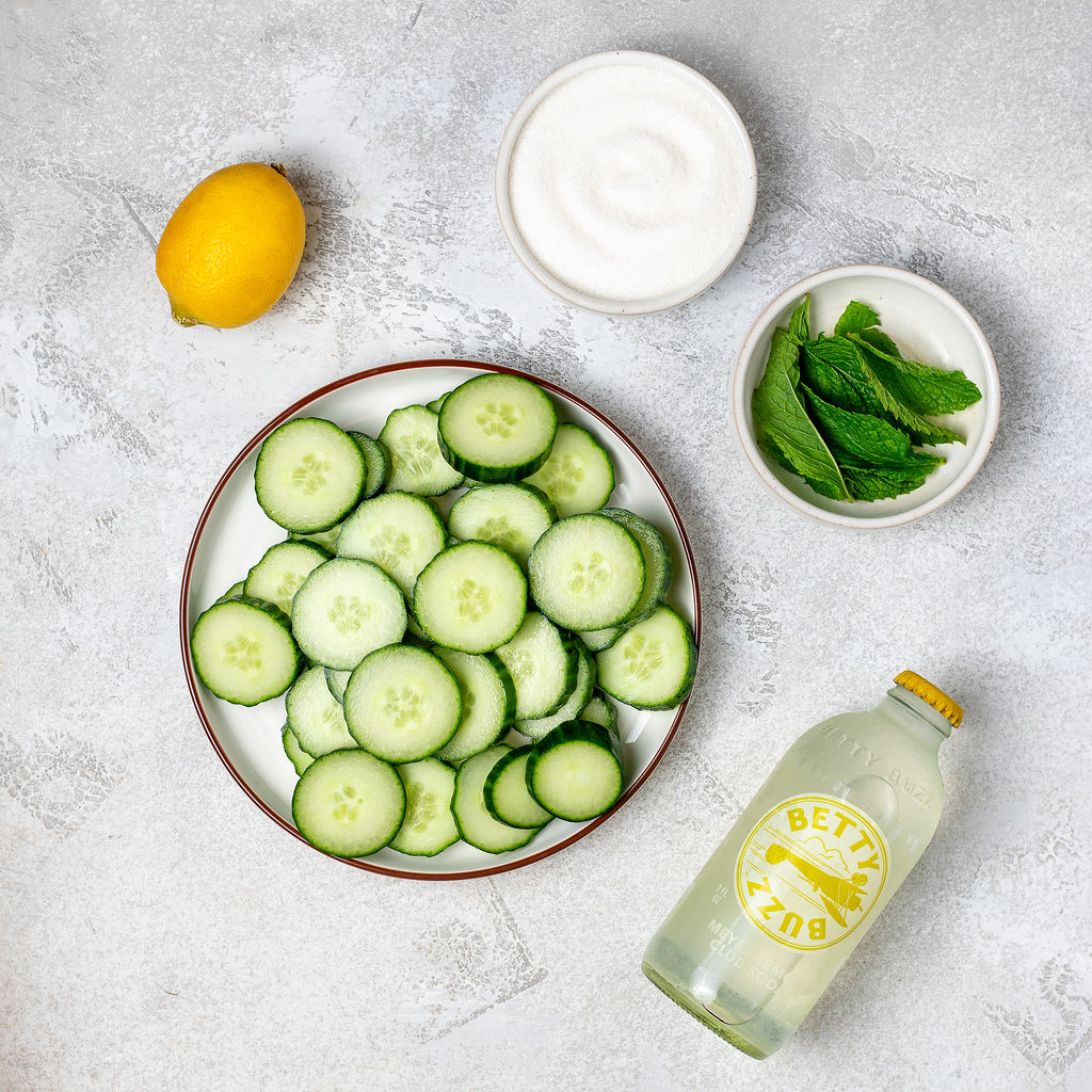 Ingredients for cucumber cooler mocktail recipe on a white marble surface.