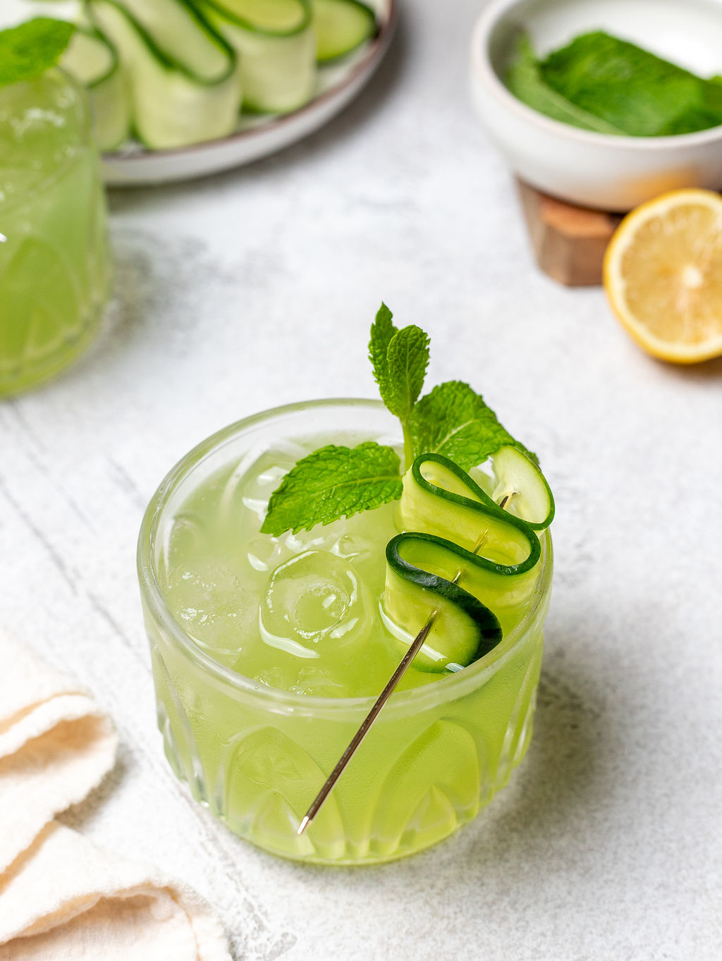 Cucumber cooler in a glass garnished with a cucumber ribbon and a sprig of mint.