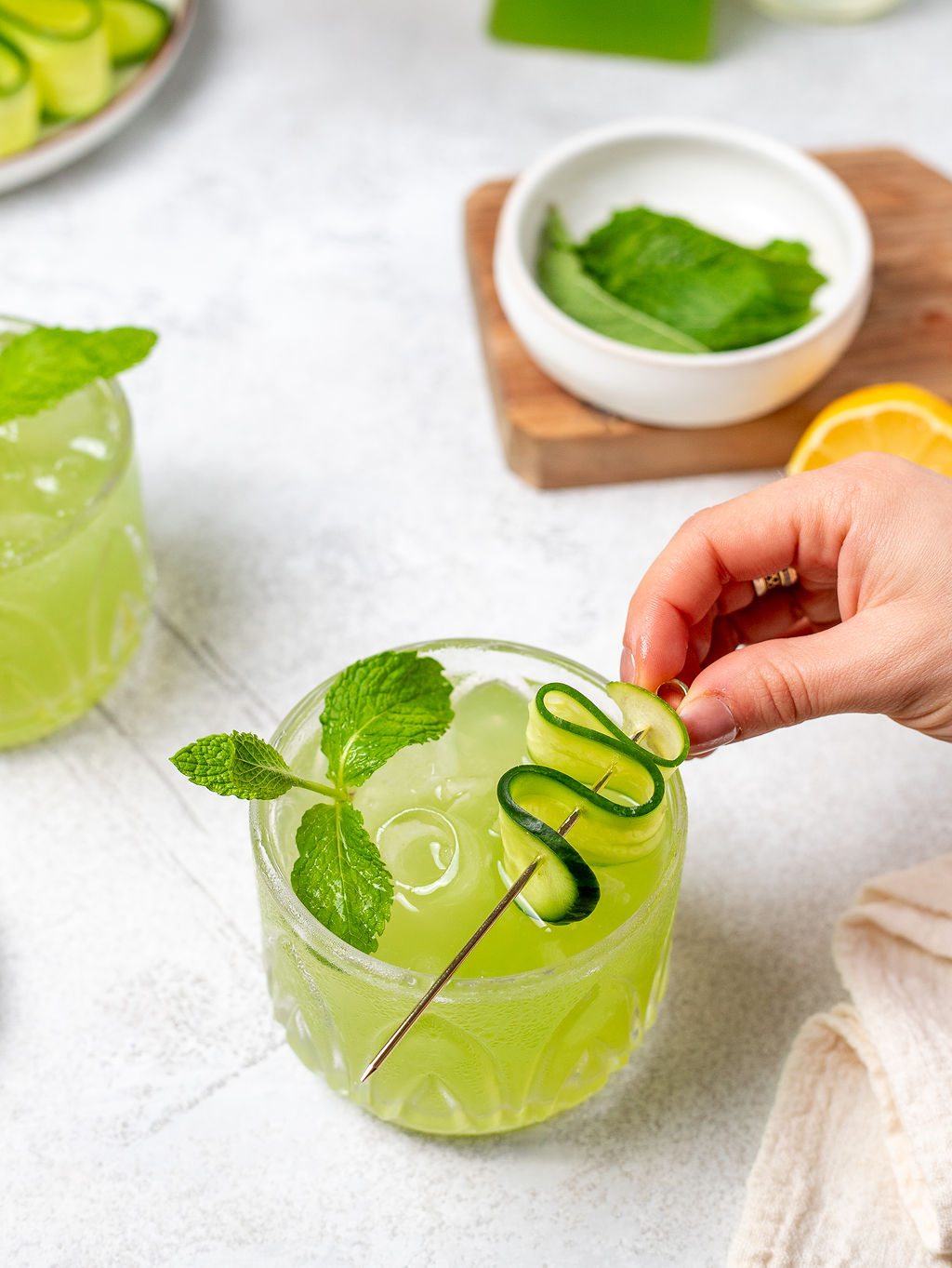A hand adding garnishes to a cucumber cooler.