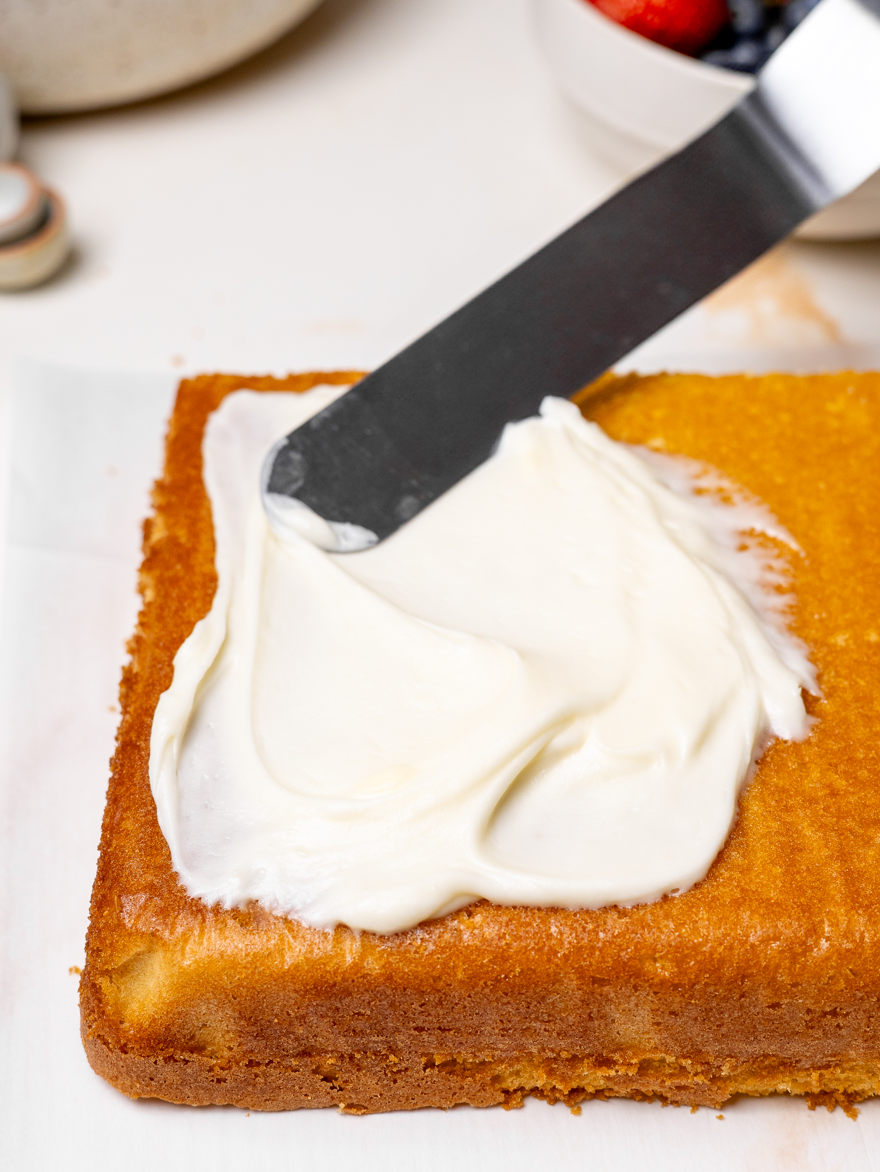 A close-up of frosting being spread onto a golden sheet cake using an offset spatula, preparing the base layer for decorating.