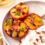 Close-up of grilled peaches garnished with mint and a side of Greek yogurt.