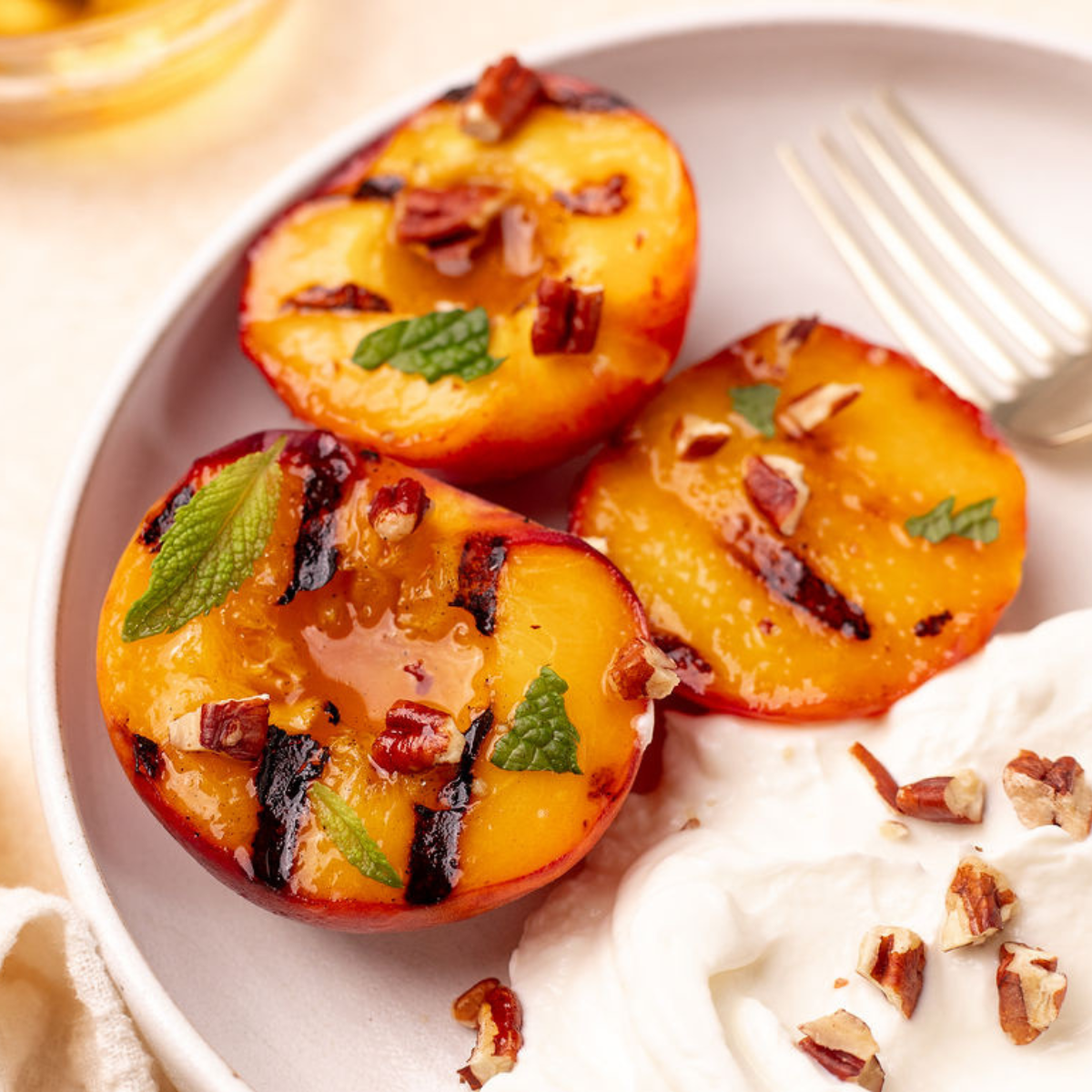 Close-up of grilled peaches garnished with mint and a side of Greek yogurt.