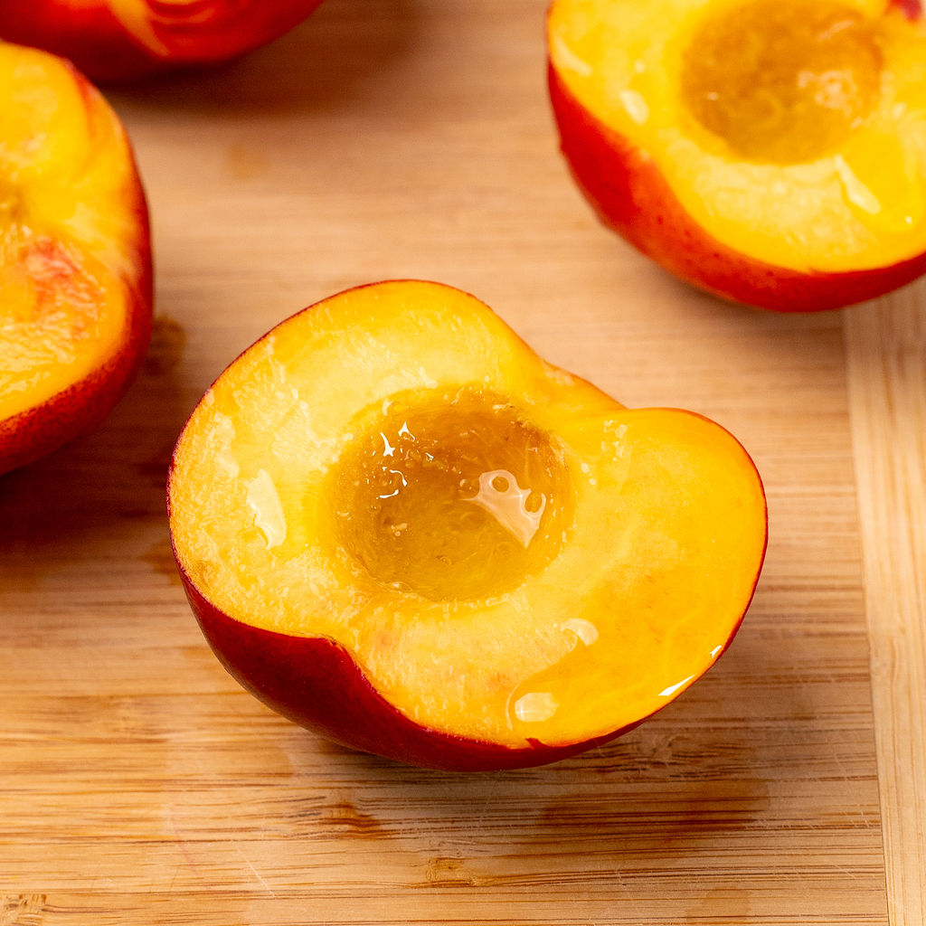 A peach cut in half on a cutting board.