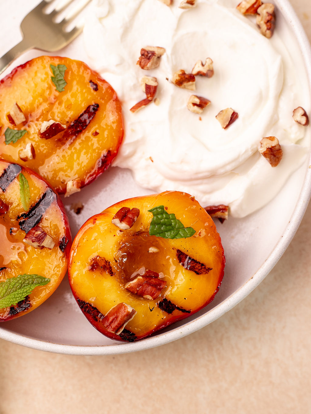 Close-up of grilled peaches garnished with mint and walnuts and a side of Greek yogurt.