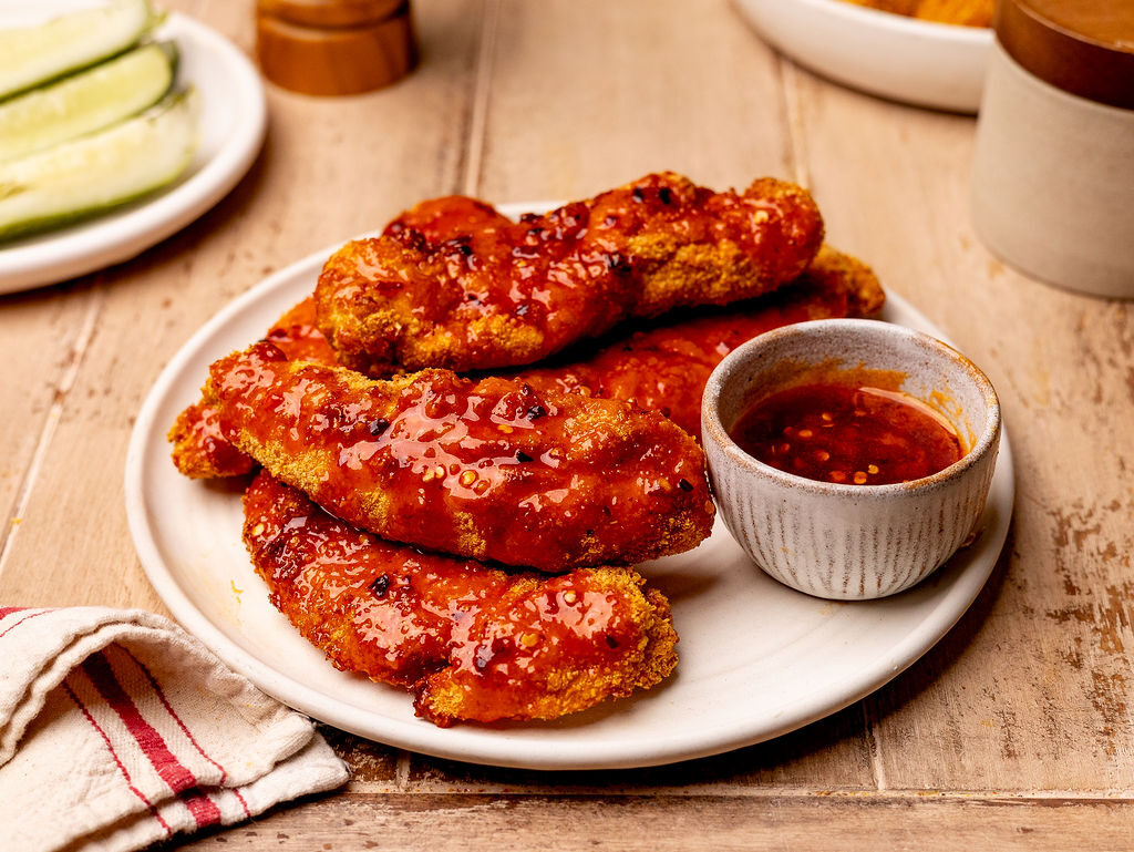 Hot honey chicken on a white plate with sauce on the side.