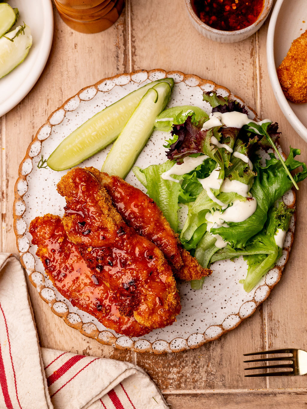 A serving of air fryer hot honey chicken on a plate with a side salad and pickles.