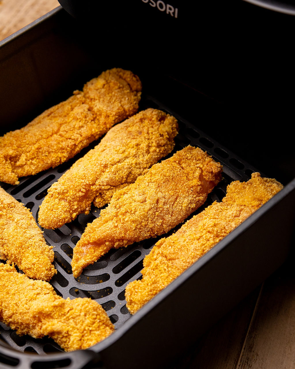 Breaded chicken tenders in an air fryer basket ready to cook.