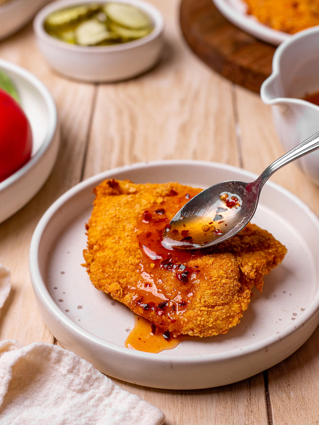 Adding hot honey sauce to breaded chicken cutlets.