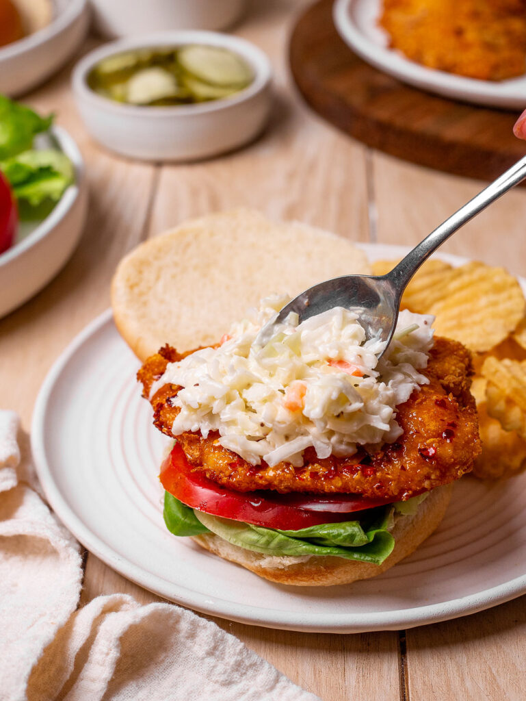 Adding a layer of coleslaw to a hot honey chicken sandwich.