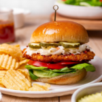 Hot honey chicken sandwich on a white plate with potato chips on the side.
