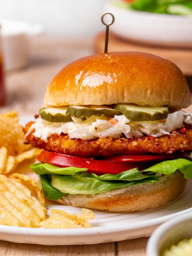Hot honey chicken sandwich on a white plate with potato chips on the side.