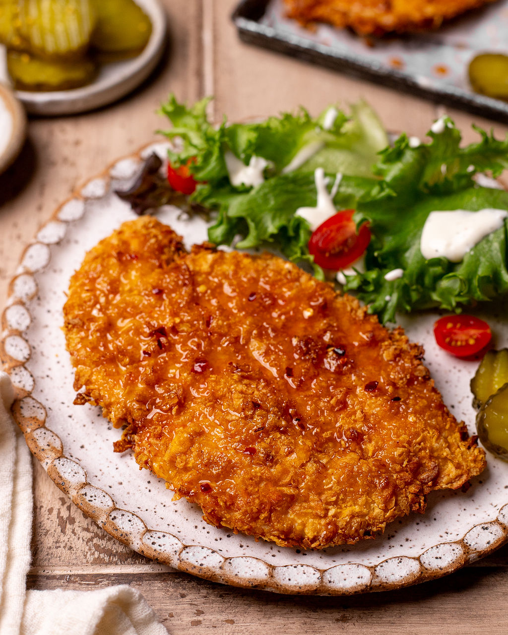 Air fryer hot honey chicken on a plate with a side salad and pickles.