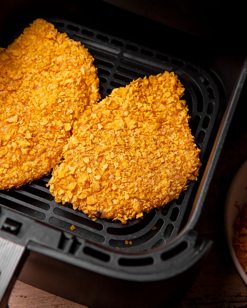 Cornflake breaded chicken breasts in an air fryer basket.