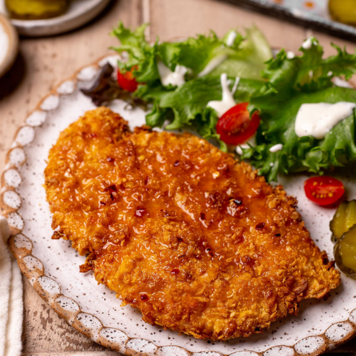 Air fryer hot honey chicken on a plate with a side salad and pickles.
