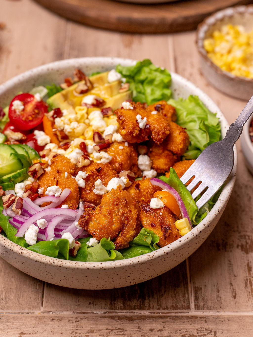 A fork dipping into hot honey chicken summer salad in a white bowl.