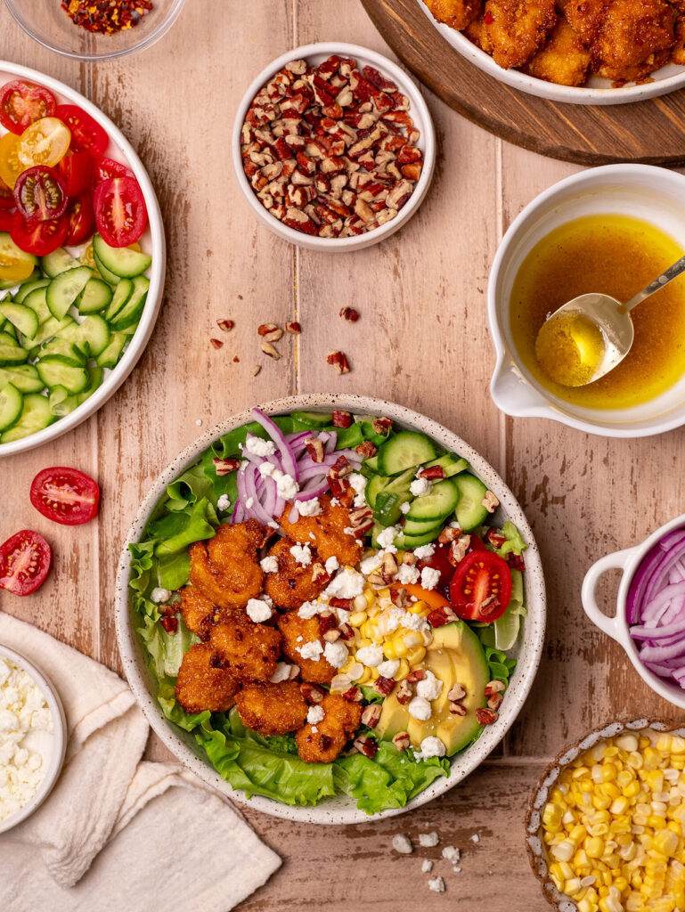 Air fryer hot honey chicken summer salad on a rustic wooden table surrounded by ingredients.
