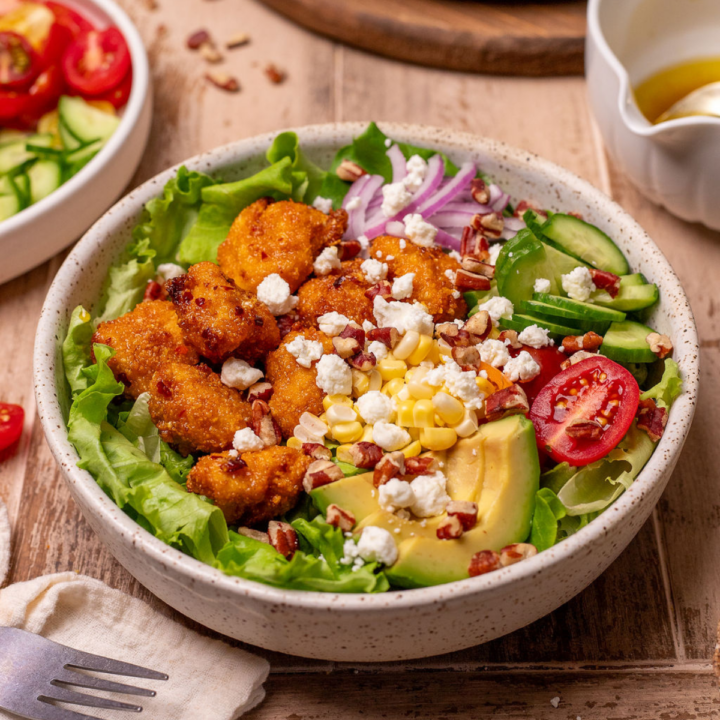 Hot honey chicken summer salad in a white bowl with feta, avocado, and almonds.