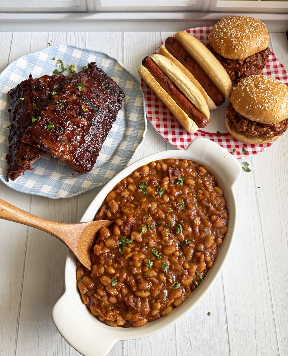 Homemade Instant Pot BBQ baked beans served with ribs, hot dogs and pulled pork sandwiches.