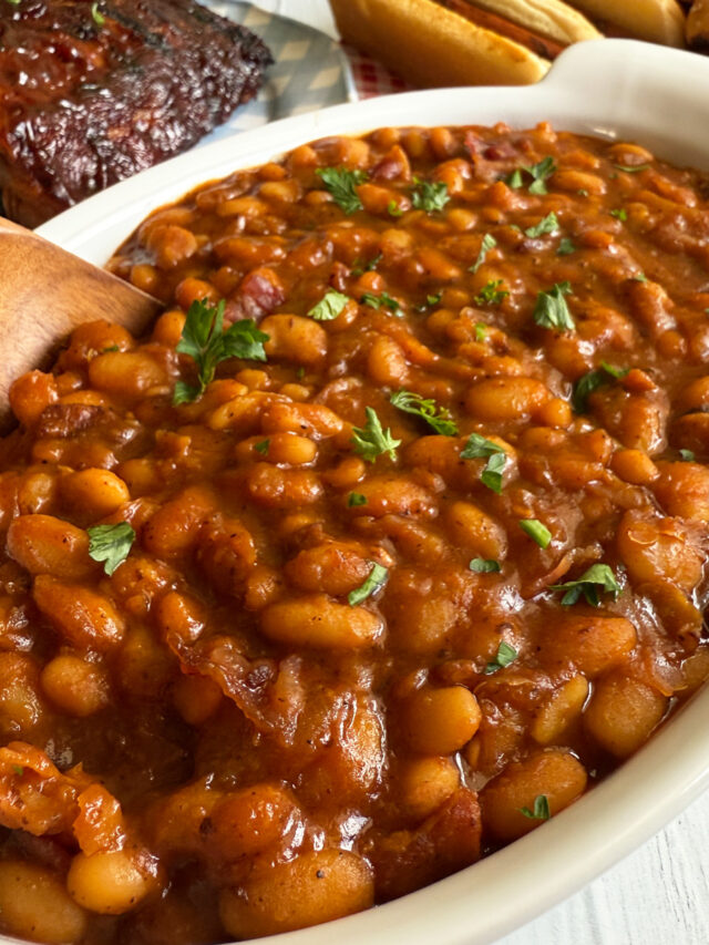 A dish of Instant Pot BBQ baked beans served with ribs, hot dogs and pulled pork sandwiches.