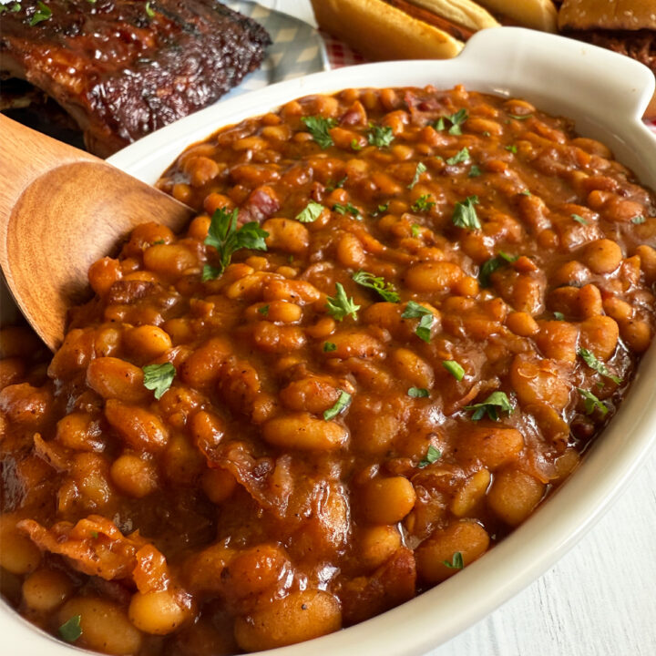 A dish of Instant Pot BBQ baked beans served with ribs, hot dogs and pulled pork sandwiches.