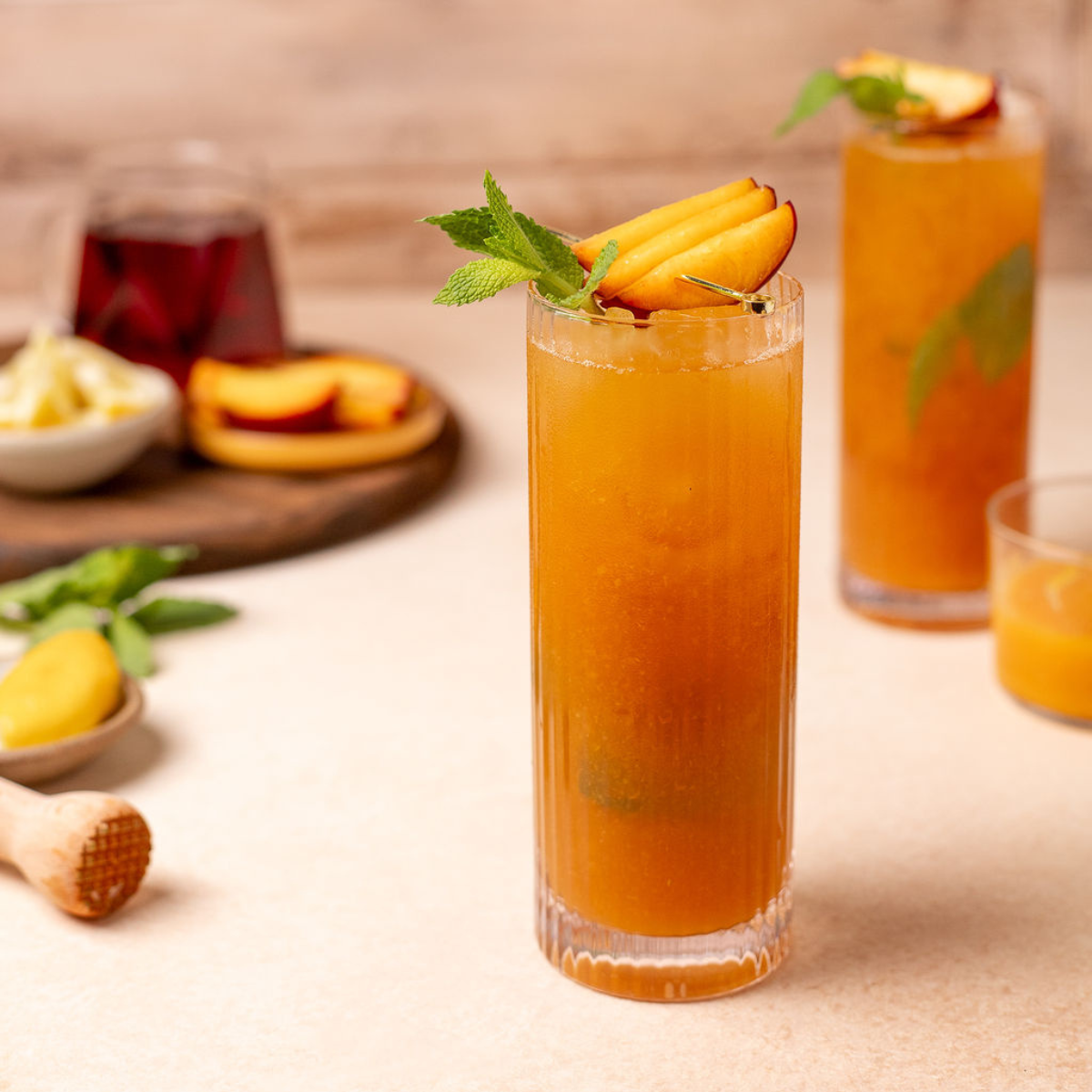 Peach and mint iced tea in a tall glass with sliced peaches and mint as a garnish.