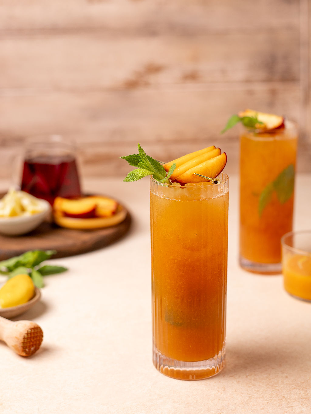 Peach and mint iced tea in a tall glass surrounded by ingredients.