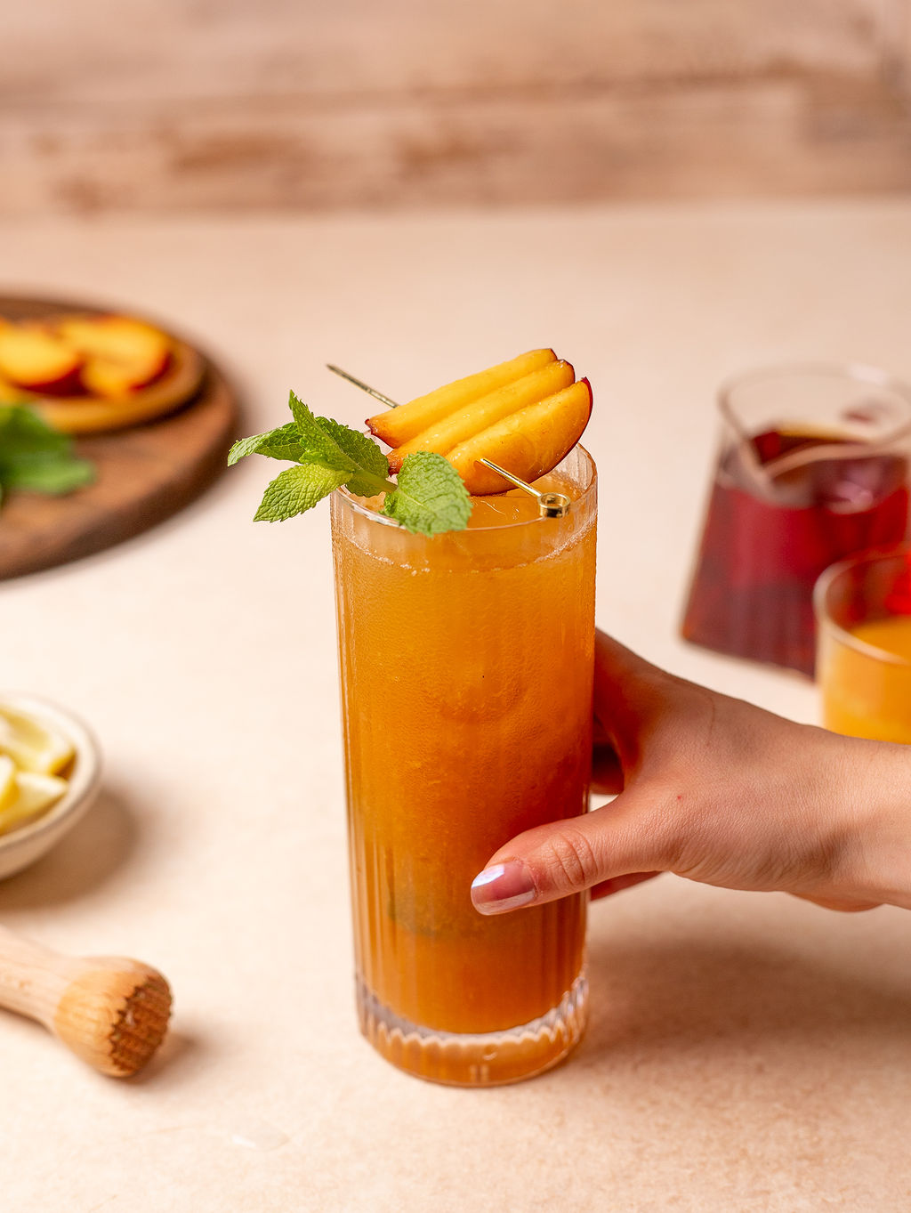 A hand holding a tall glass of peach and mint iced tea.