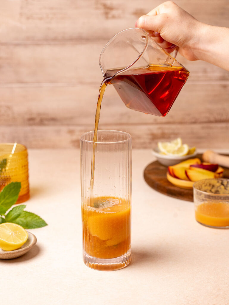 Pouring black tea into a tall glass.