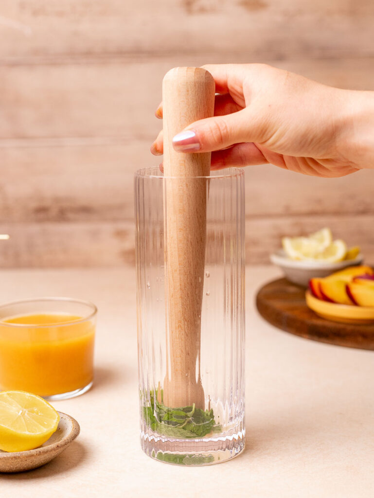 Muddling mint and lemon together to make a peach and mint iced tea.