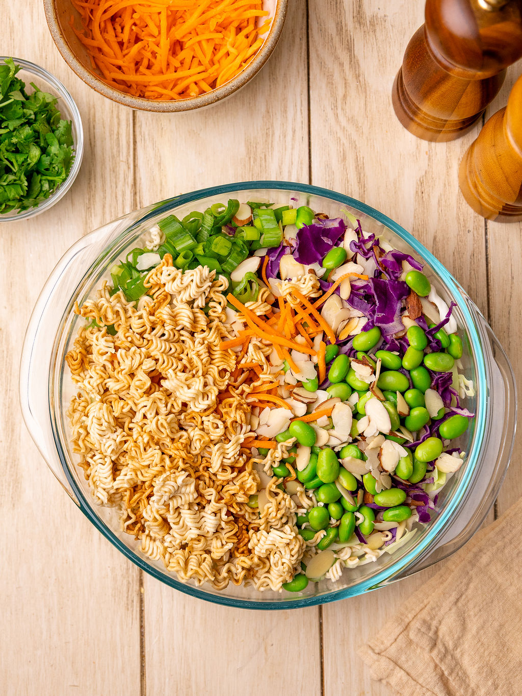Ingredients for ramen noodle salad in a glass mixing bowl before tossing.