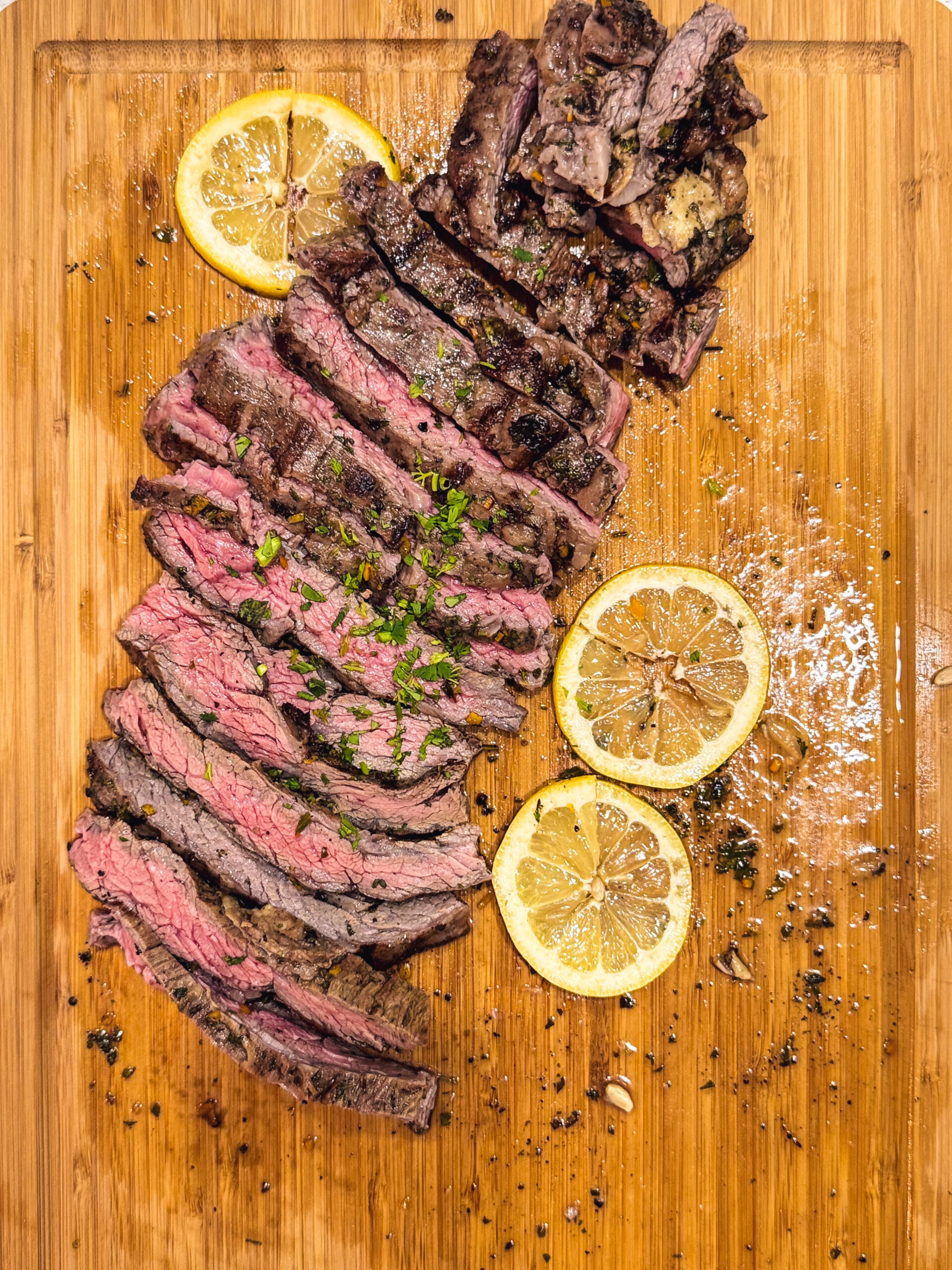 Aerial view of sliced skirt steak on a cutting board with sliced lemon on the side.