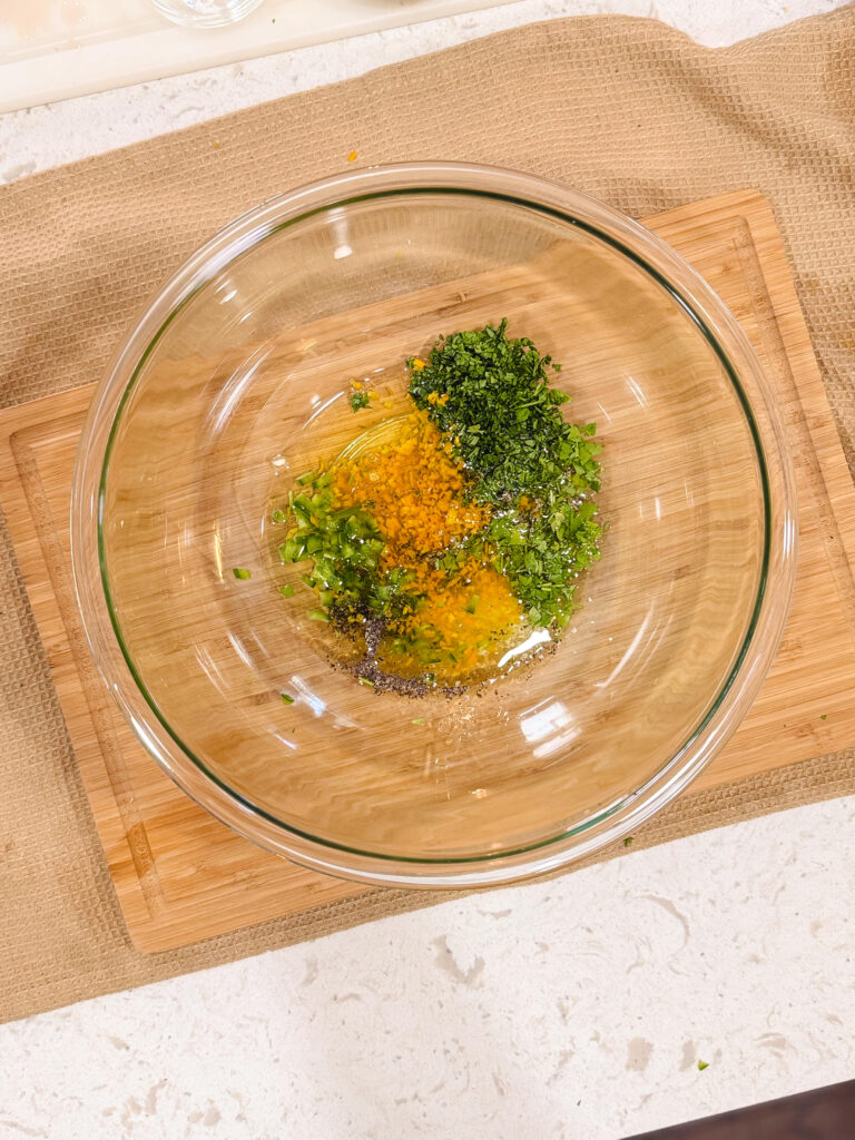 Ingredients for chimichurri marinade in a glass bowl over a wooden cutting board.