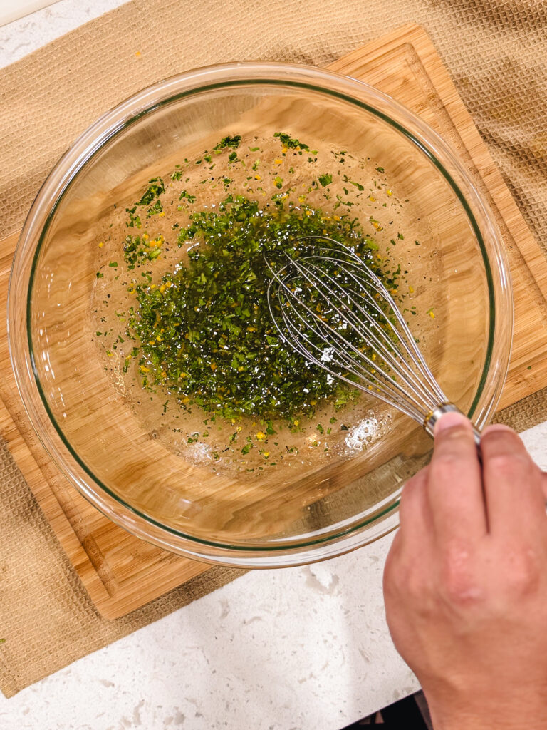 Whisking the chimichurri marinade in a glass mixing bowl.