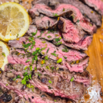Close up of sliced skirt steak with chimichurri sauce over a wooden cutting board with a side of lemon.