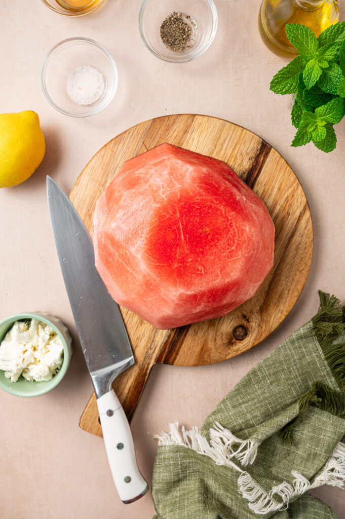Fresh, skin-off watermelon on a cutting board surrounded by ingredients.