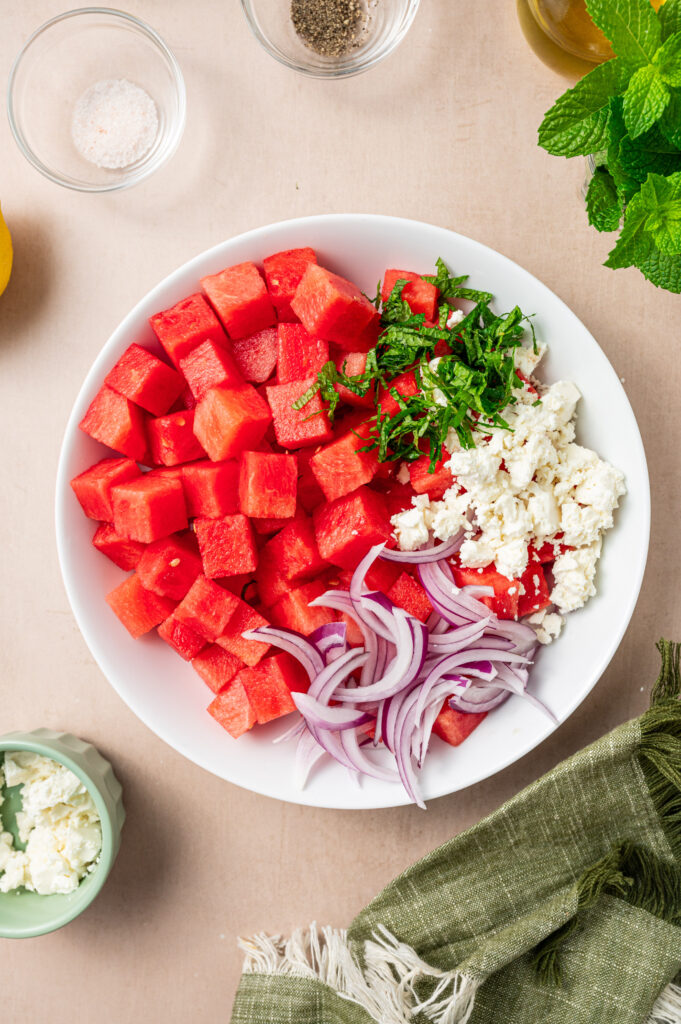 Cubed watermelon with feta, mint, and red onion in a bowl before mixing.