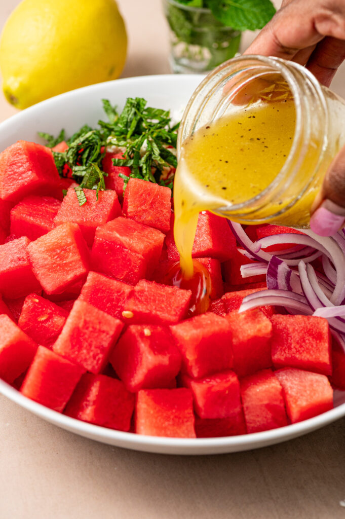 Pouring lemon-honey dressing in a bowl of cubed watermelon.