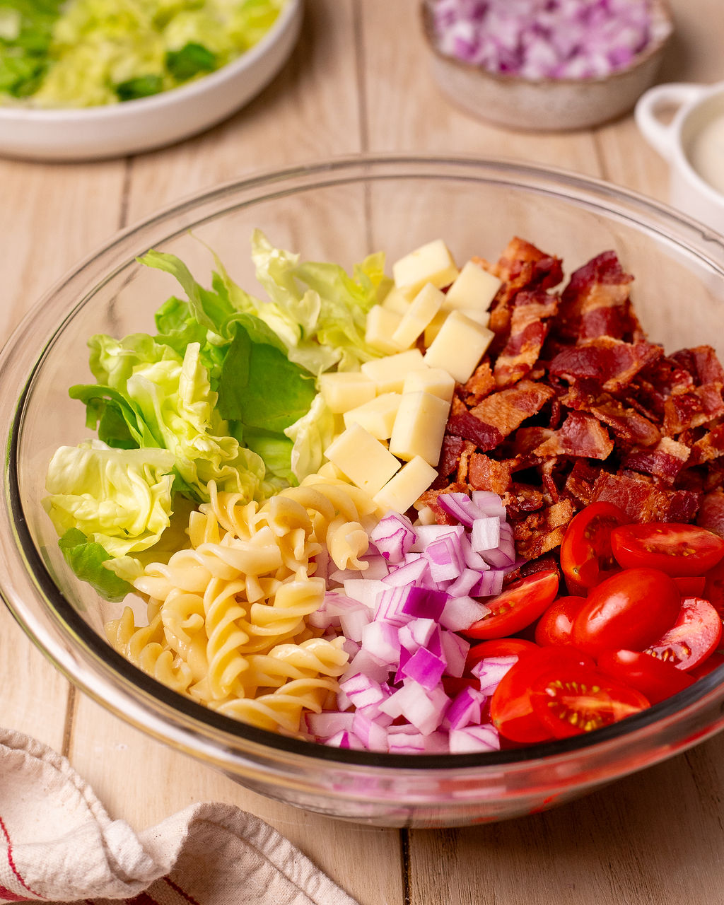 All the elements of a BLT pasta salad in a glass bowl before getting mixed.