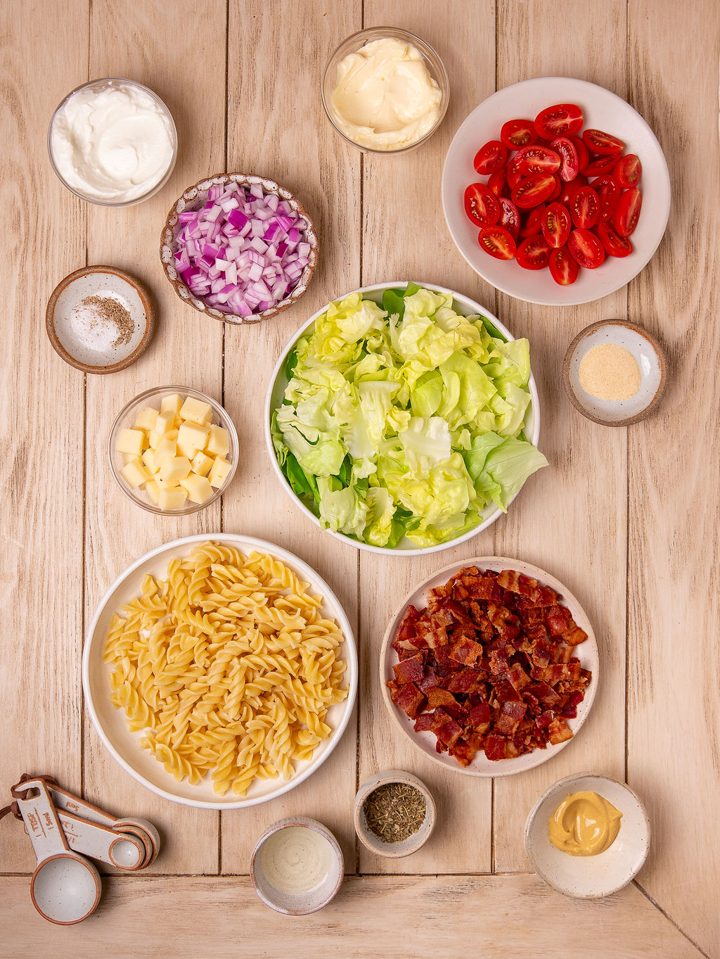 Ingredients for BLT pasta salad on a light wooden surface.