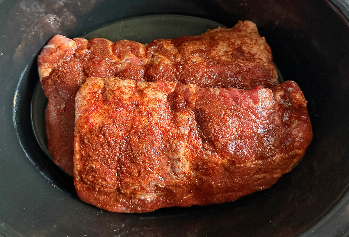 Seasoned baby back ribs place in a slow cooker.