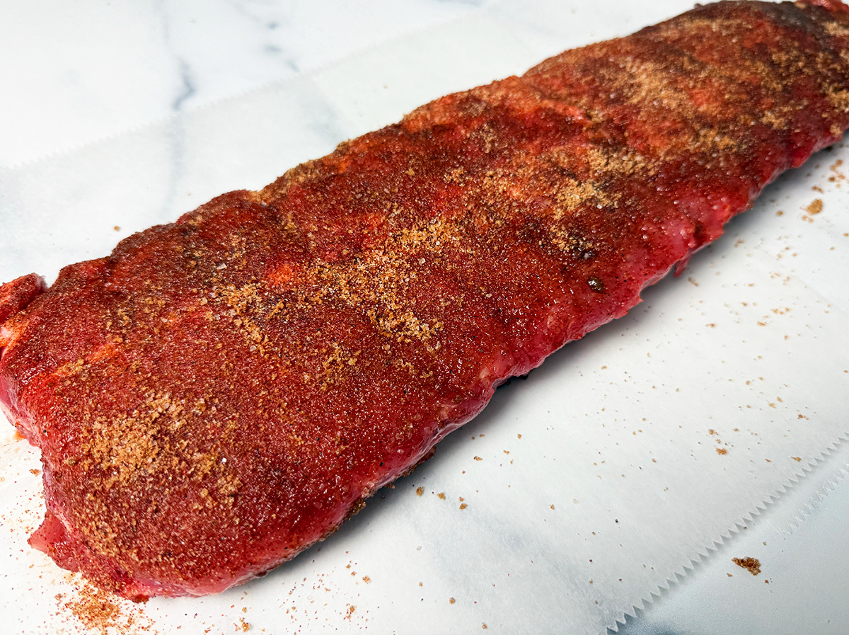 Seasoning a slab of ribs to cook in a slow cooker.