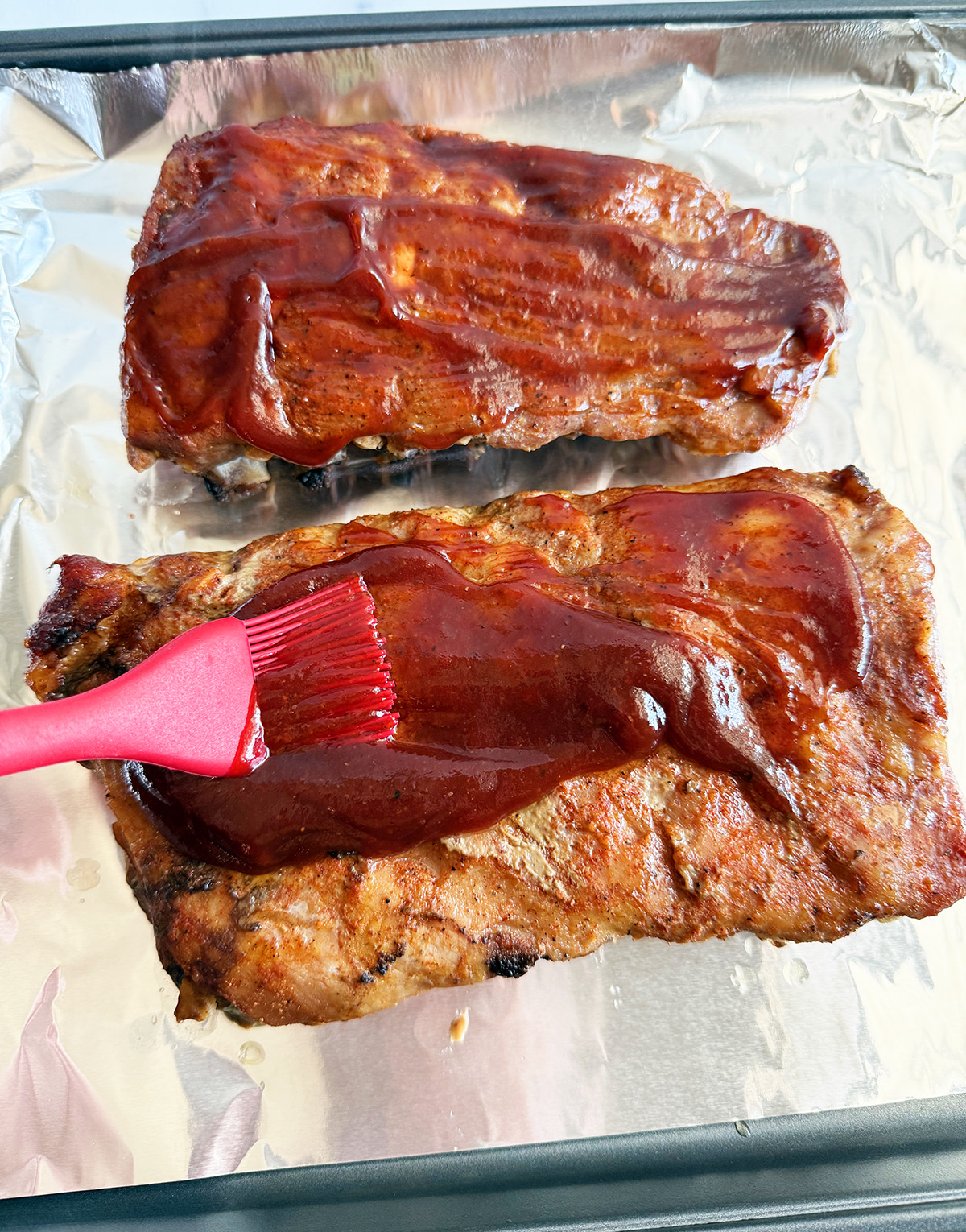 Brushing BBQ sauce on ribs before broiling.