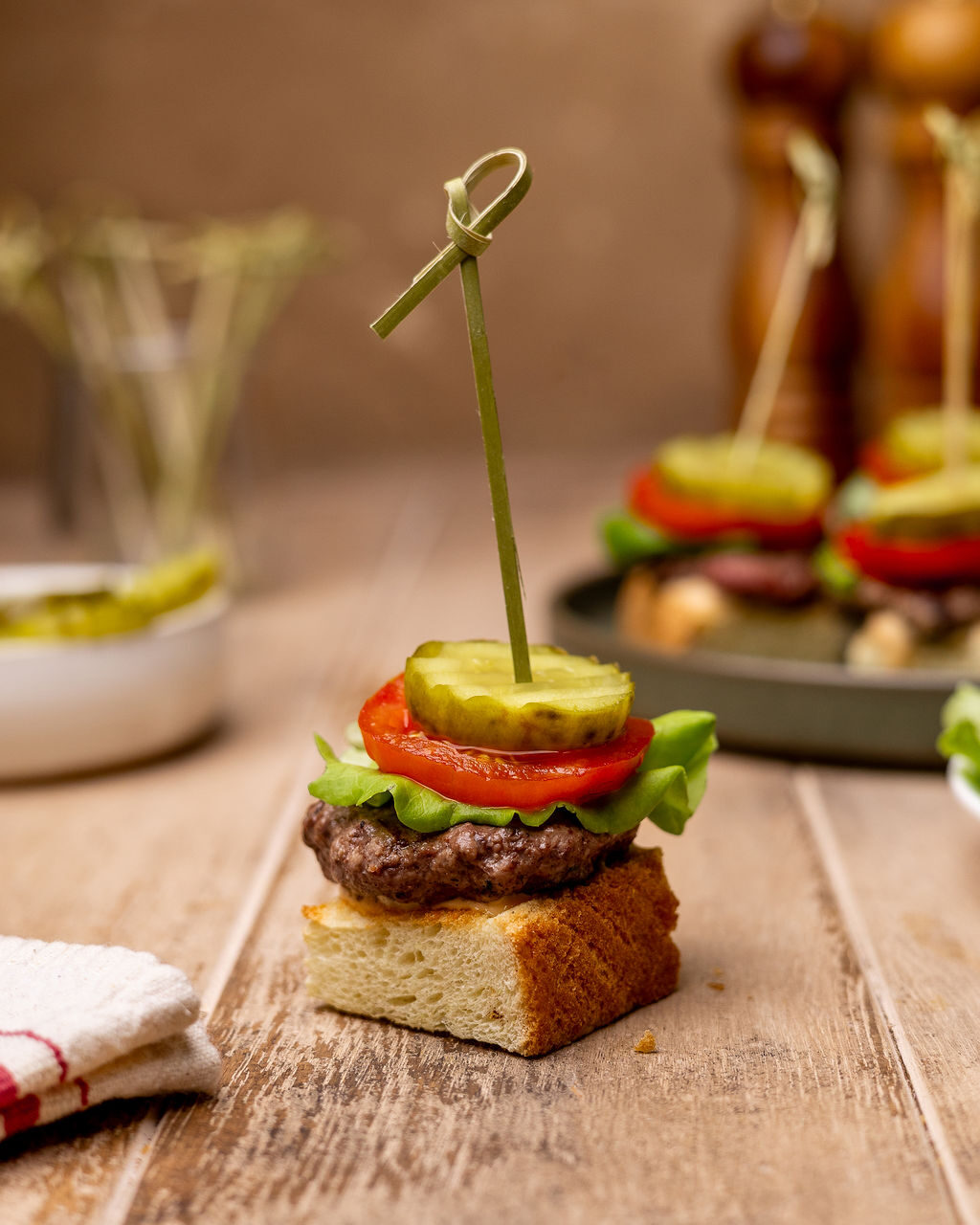 A burger skewer with tomato, pickles, and lettuce.