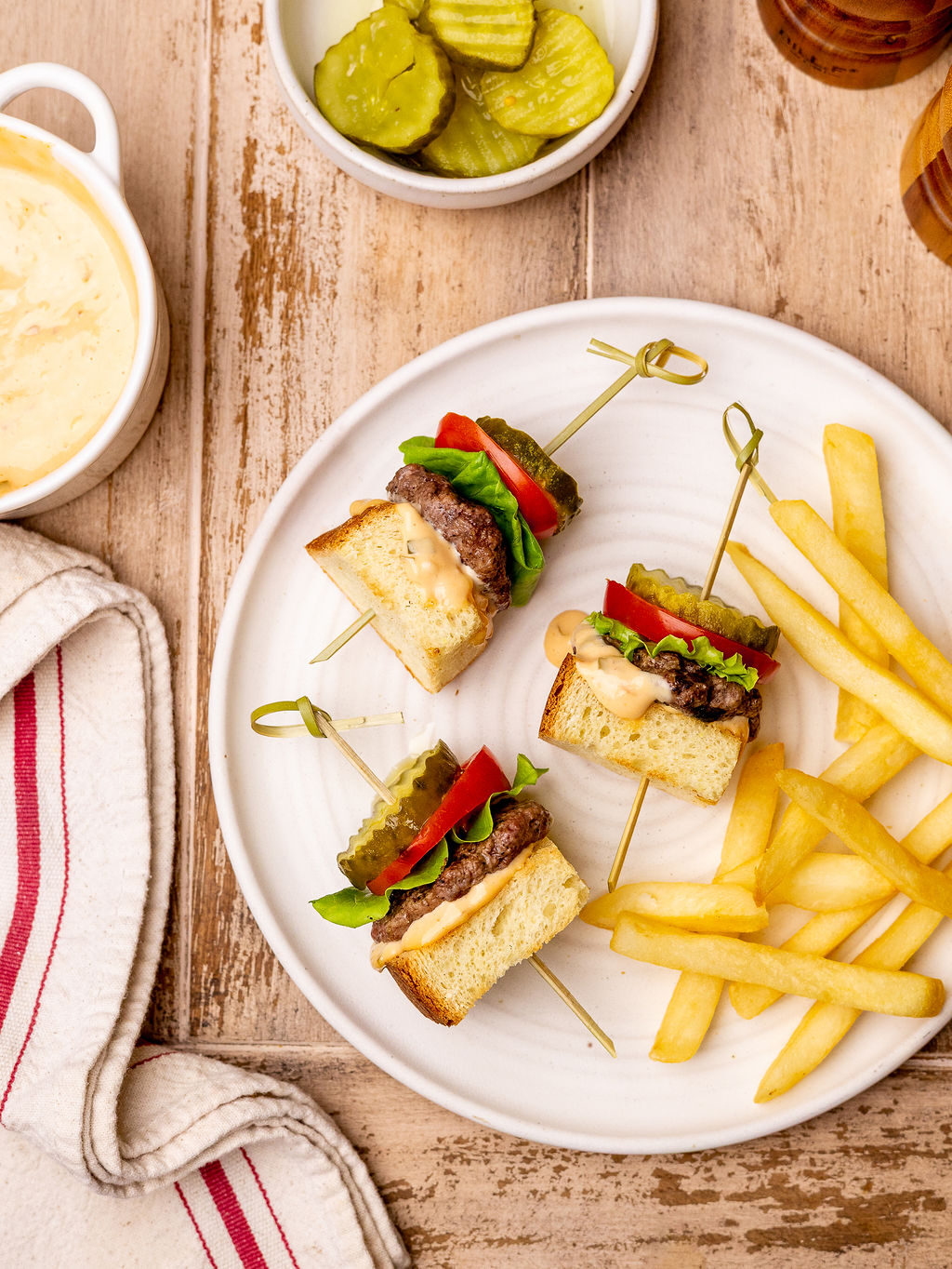 A serving of grilled burger skewers on a white plate served with French fries.