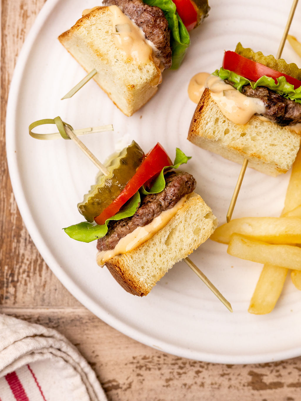 Close-up of grilled burger skewers on a white plate served with French fries.