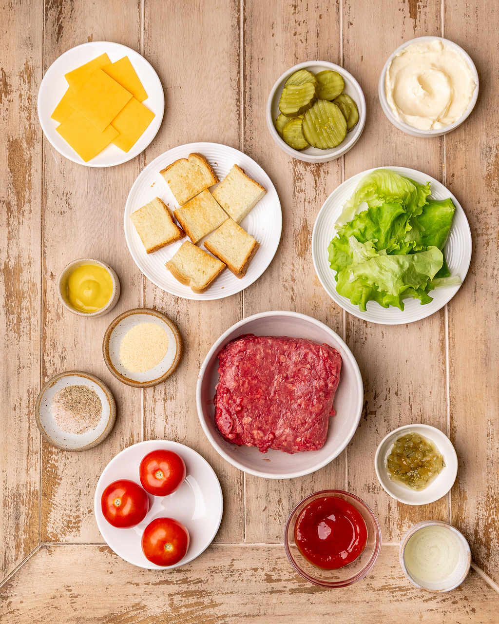 Ingredients for grilled burger skewers on a light wooden surface.