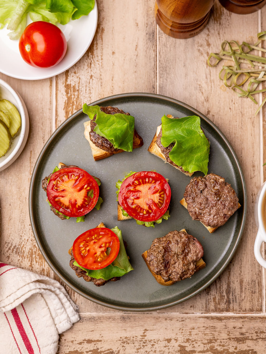 Assembling burger patties on a black plate with tomatoes and lettuce.