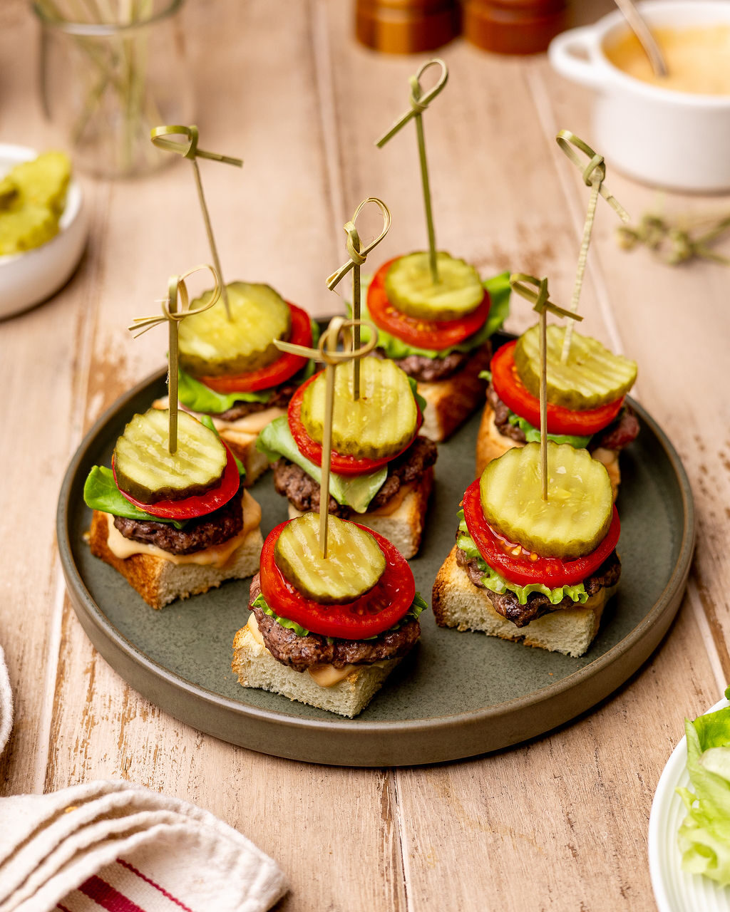 Grilled burger skewers on a black plate with lettuce, tomatoes, and pickles.