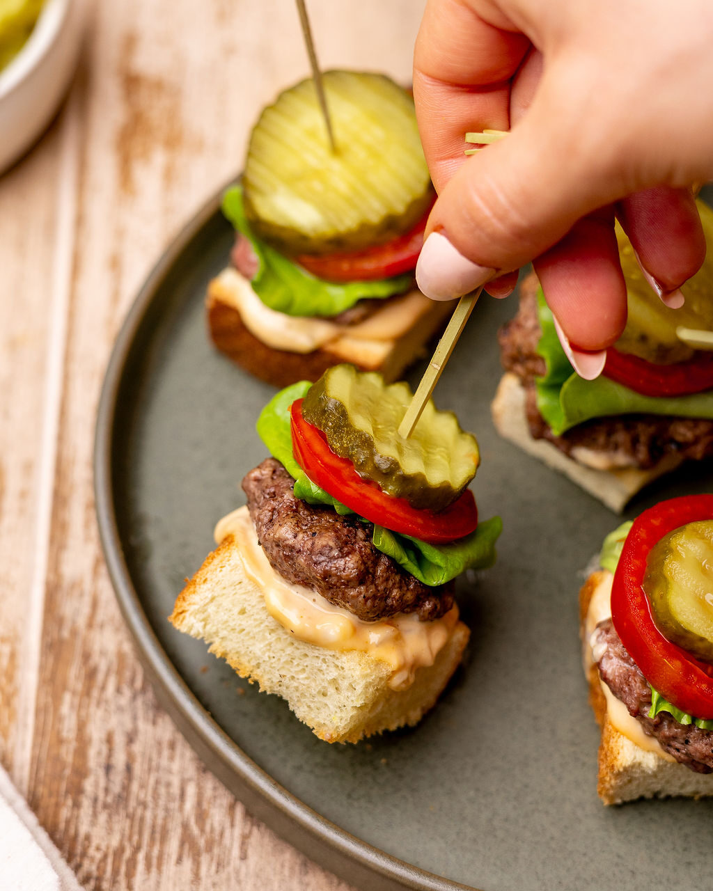 A hand grabbing a grilled burger skewer.